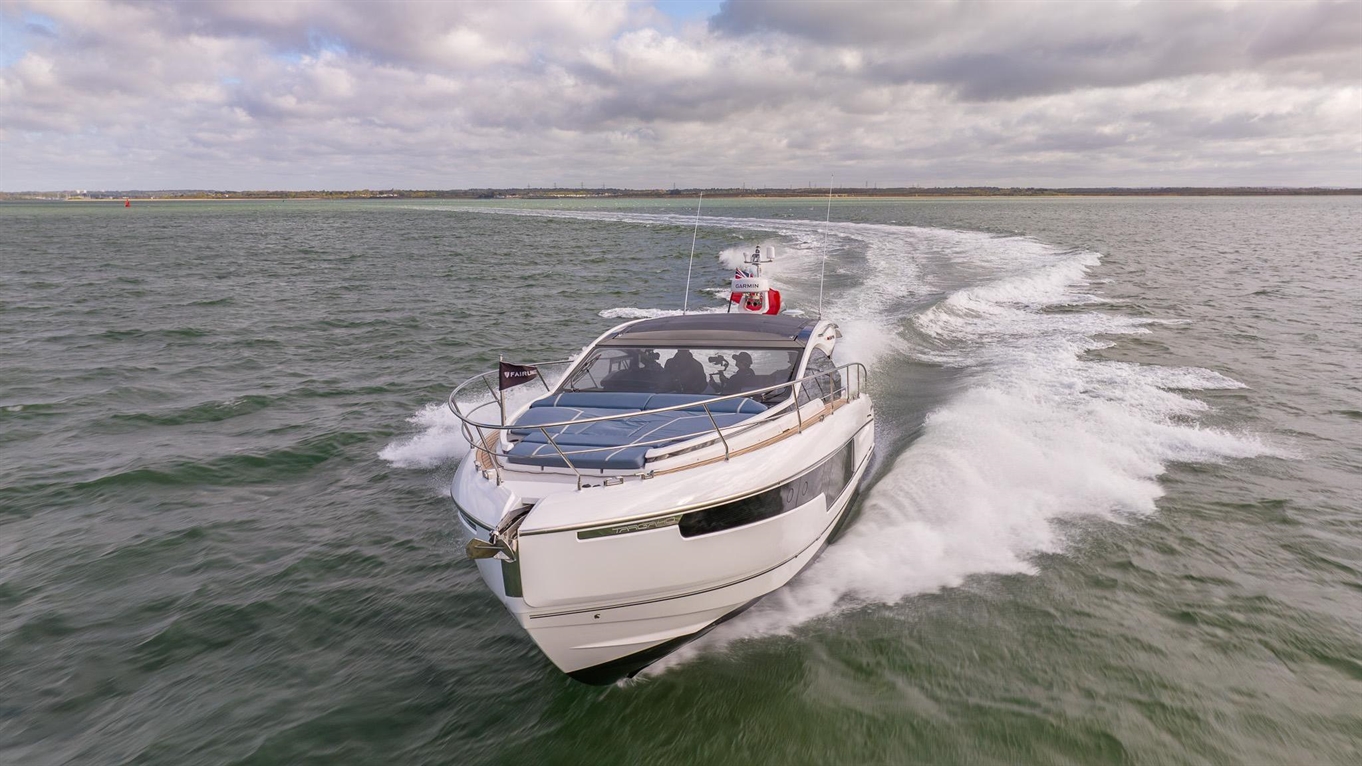 A sleek white motorboat speeds through green waters with waves trailing behind, under a partly cloudy sky.